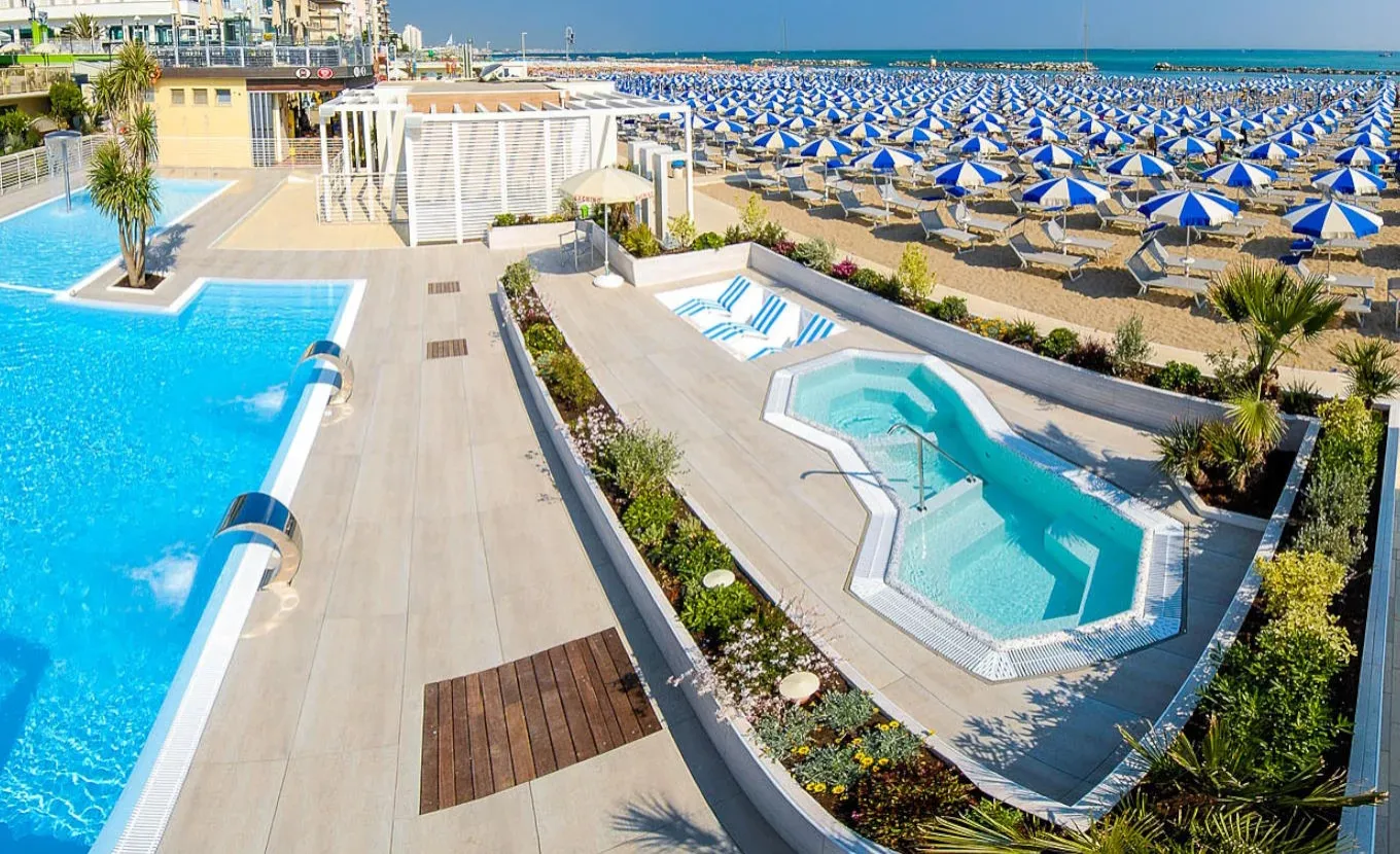 Piscina e idromassaggio vicino alla spiaggia con ombrelloni blu e bianchi.