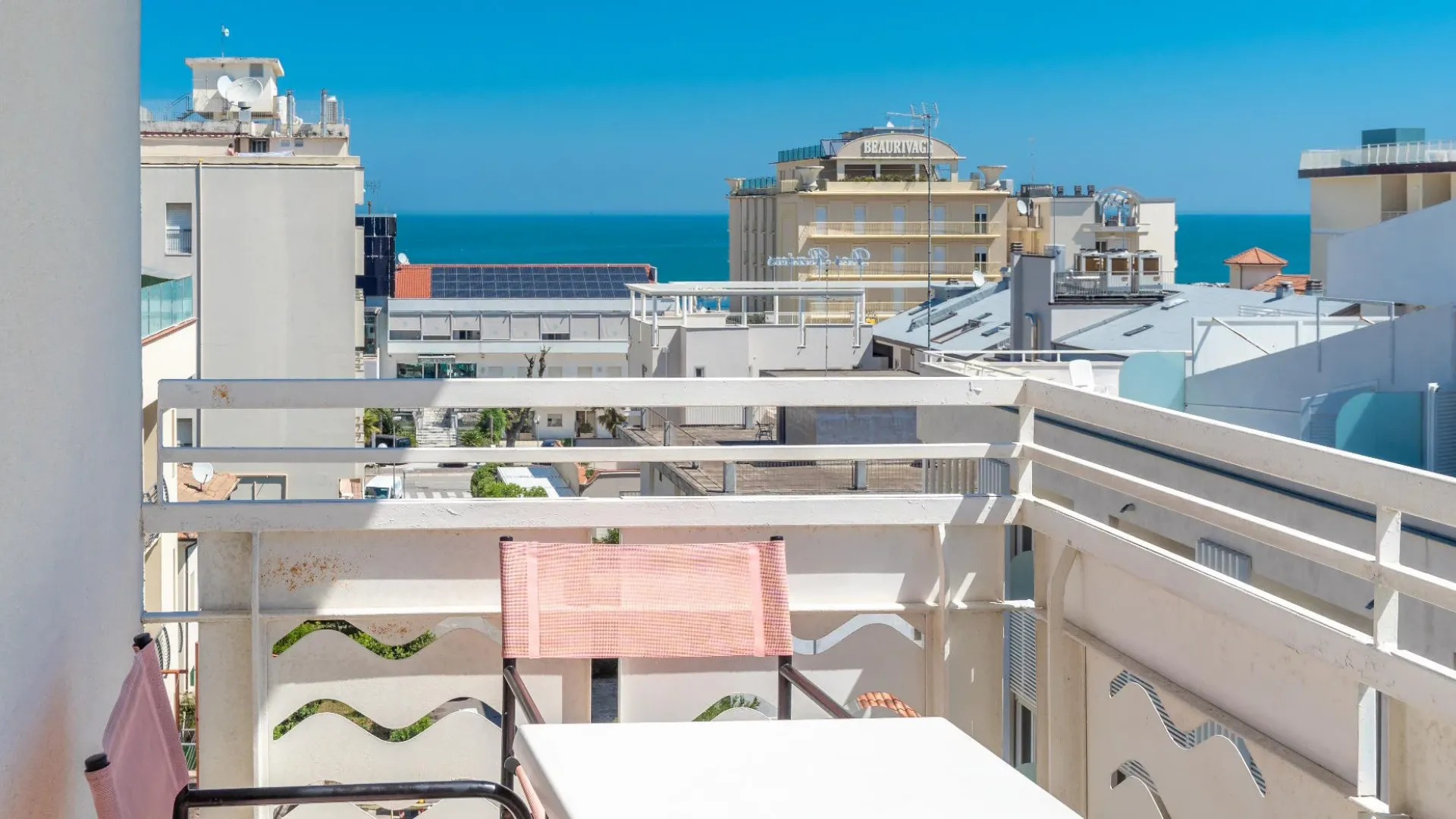 Balcone con vista sul mare, circondato da edifici, con sedie e tavolo.