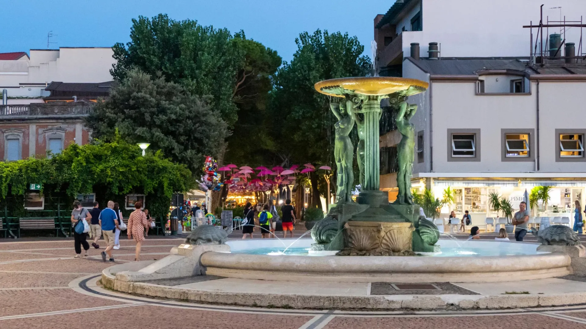 Piazza con una fontana al centro, circondata da edifici e persone passeggianti.