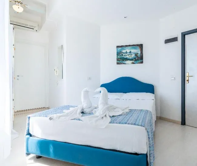 Camera luminosa con letto matrimoniale, decorazioni bianche e blu, asciugamani piegati a forma di cigno.