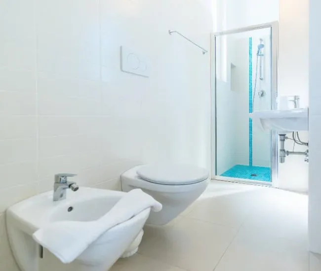 Bagno moderno con doccia, bidet e WC sospesi, piastrelle bianche e dettagli blu.