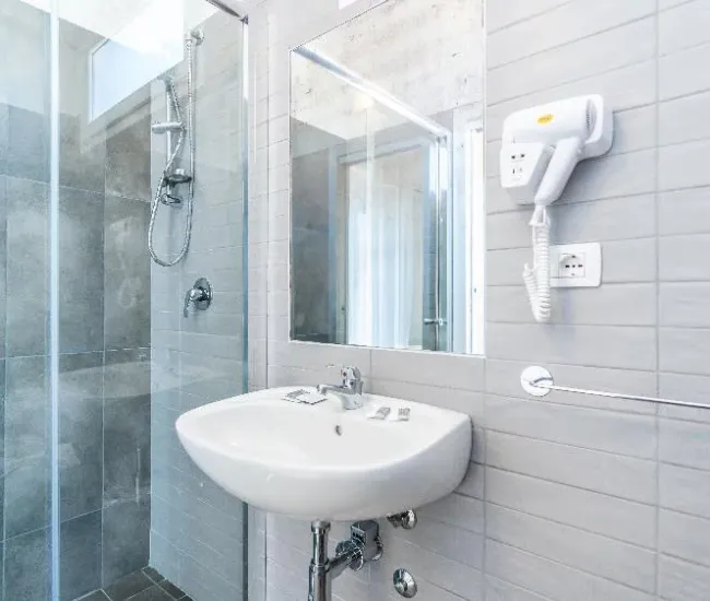 Bagno moderno con doccia, lavabo, specchio e asciugacapelli a parete.