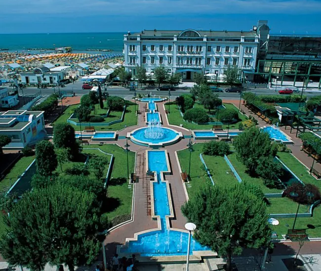 Giardino con fontane, vicino alla spiaggia, circondato da edifici e strutture turistiche.