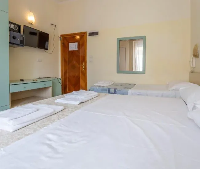 Camera d'albergo con letti, TV, cassaforte e specchio, arredata in stile semplice.