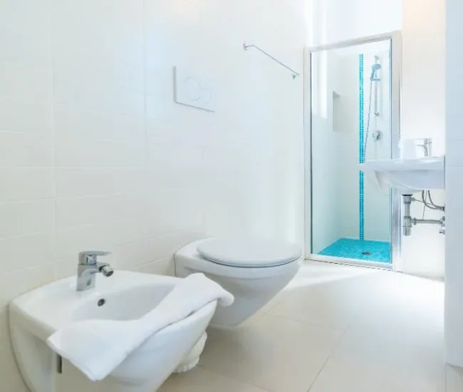 Bagno moderno con bidet, WC, doccia e lavabo, arredato in bianco con dettagli blu.