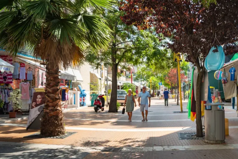 Strada pedonale con negozi, palme e persone che passeggiano in una giornata soleggiata.
